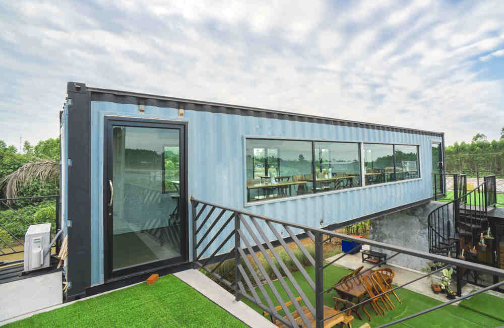 A blue container house with a deck and patio.